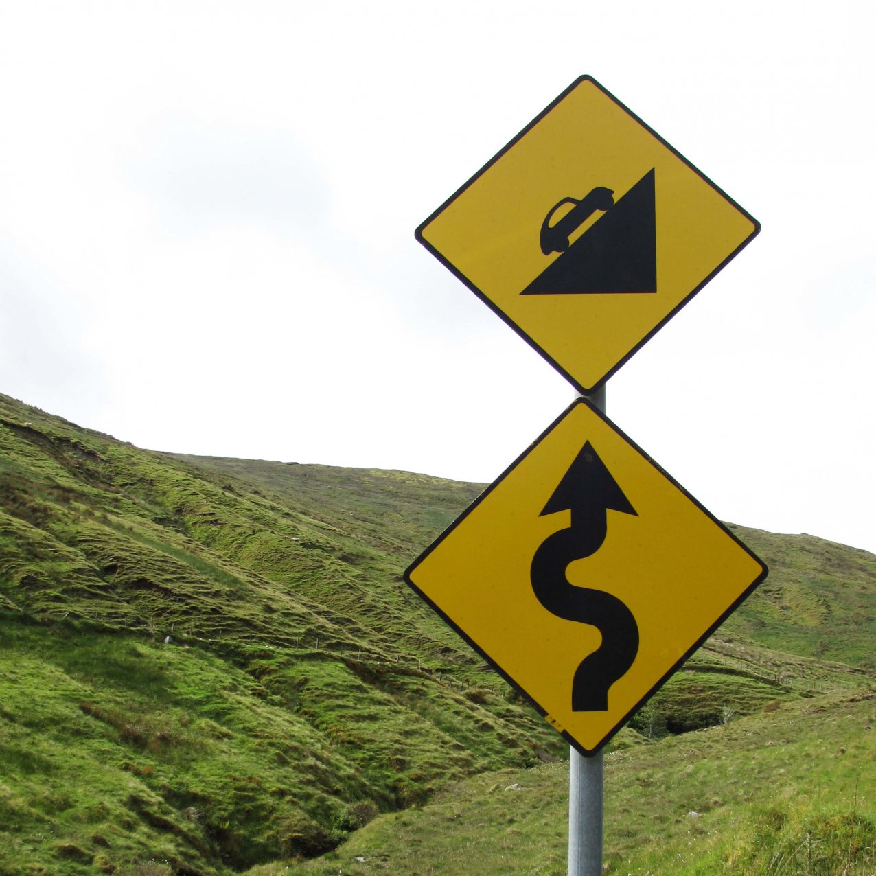 Roadsigns indicating a twisting, uphill climb ahead, with green hills in the background, somewhere in Ireland